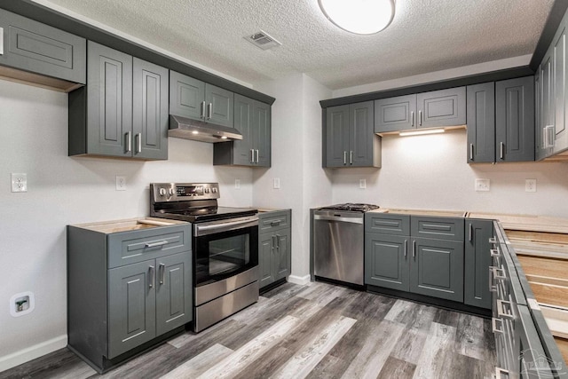7125 Ben Sasser Dr, Pensacola, FL 32526 - kitchen featuring stainless steel appliances, under cabinet range hood, light countertops, wood finished floors, and a textured ceiling