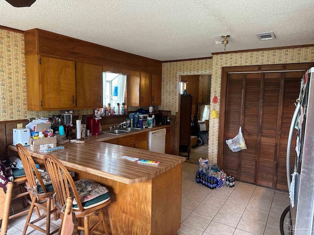 2939 Sundance Ln, Cantonment, FL 32533 - kitchen featuring wallpapered walls, stainless steel refrigerator, a textured ceiling, brown cabinetry, and white dishwasher