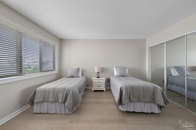 bedroom featuring a closet, a textured ceiling, baseboards, and light wood-style floors
