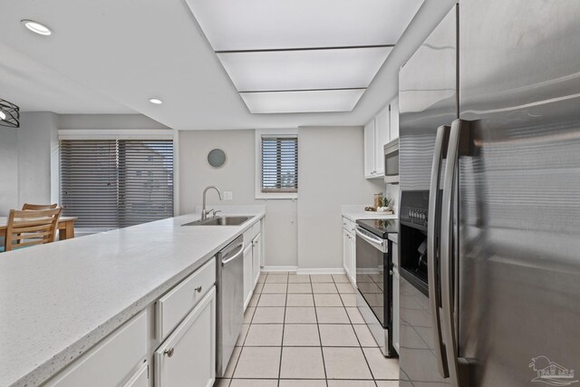 kitchen featuring appliances with stainless steel finishes, a sink, white cabinets, light tile patterned floors, and baseboards