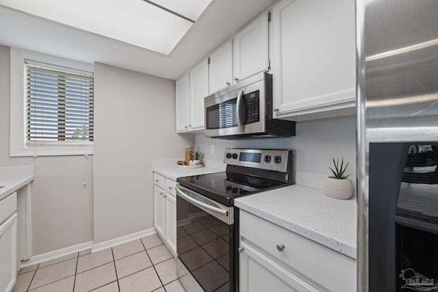kitchen featuring appliances with stainless steel finishes, white cabinetry, light tile patterned flooring, baseboards, and light stone counters