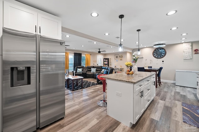 kitchen with light stone countertops, a center island, light wood-style flooring, and stainless steel fridge with ice dispenser