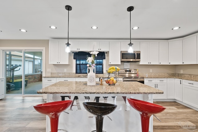 kitchen with light wood-type flooring, a center island, white cabinetry, stainless steel appliances, and a breakfast bar area