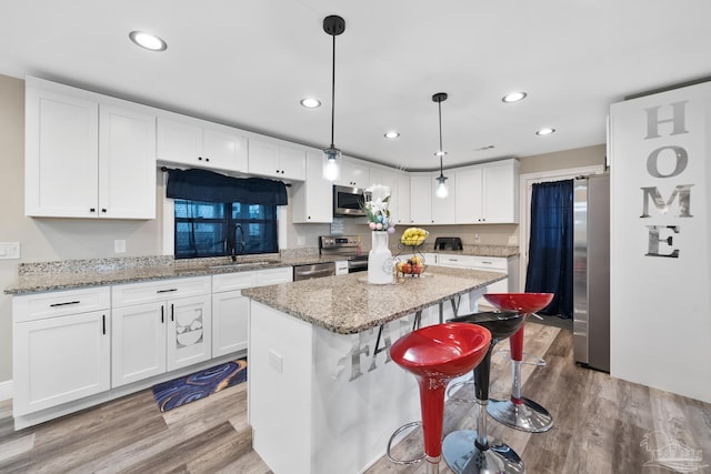 kitchen featuring a sink, wood finished floors, a center island, white cabinetry, and stainless steel appliances