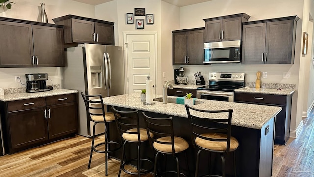 kitchen featuring dark brown cabinets, an island with sink, stainless steel appliances, and light hardwood / wood-style floors