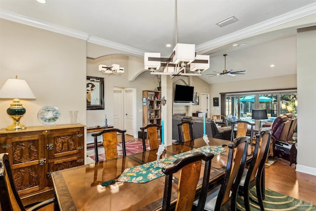 dining area featuring wood-type flooring, ceiling fan with notable chandelier, vaulted ceiling, and crown molding