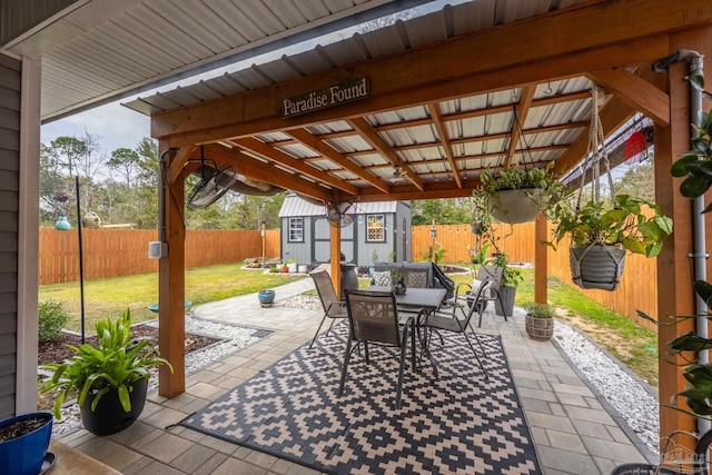 view of patio / terrace with an outbuilding, outdoor dining area, a fenced backyard, and a shed