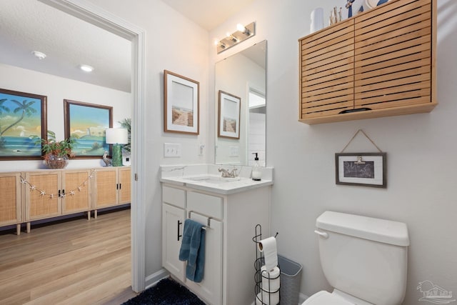 half bathroom featuring toilet, wood finished floors, and vanity