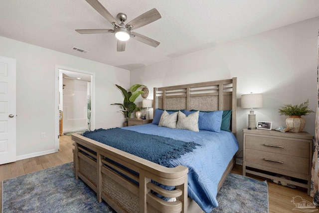 bedroom with a textured ceiling, wood finished floors, visible vents, and baseboards