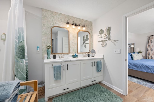 ensuite bathroom with double vanity, wood finished floors, a sink, and baseboards