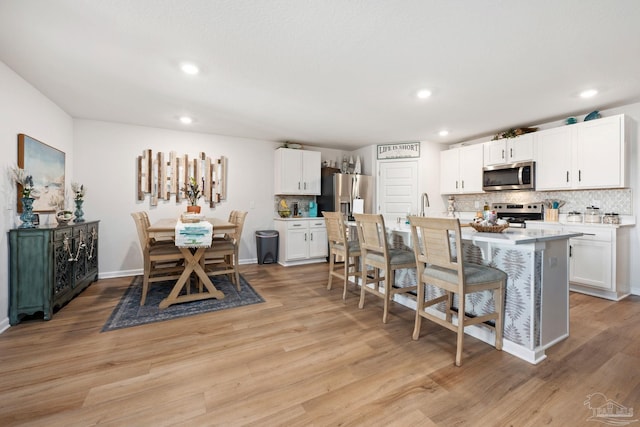 kitchen featuring a breakfast bar, light wood finished floors, stainless steel appliances, light countertops, and backsplash