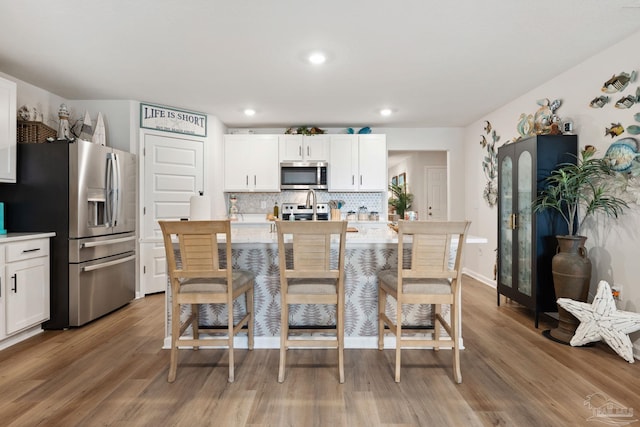 kitchen with stainless steel appliances, tasteful backsplash, light countertops, white cabinets, and light wood-type flooring