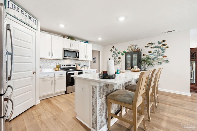 kitchen featuring stainless steel appliances, tasteful backsplash, visible vents, light wood-style floors, and white cabinets