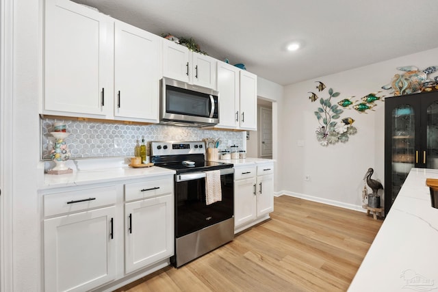 kitchen with white cabinets, appliances with stainless steel finishes, light stone countertops, light wood finished floors, and tasteful backsplash