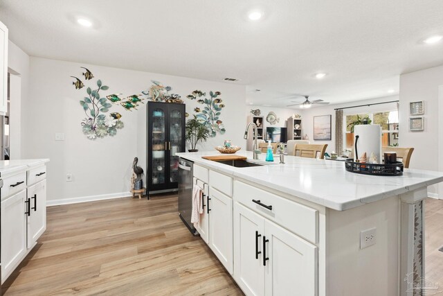 kitchen featuring white cabinets, dishwasher, a kitchen island with sink, light wood-style floors, and a sink