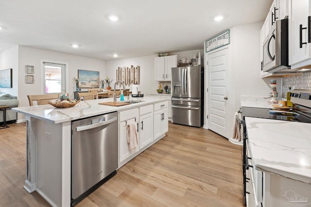 kitchen featuring light wood-style flooring, a sink, appliances with stainless steel finishes, light stone countertops, and an island with sink