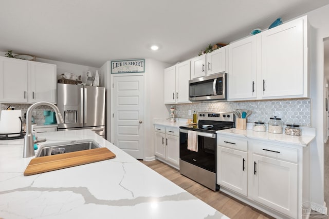 kitchen with light wood finished floors, tasteful backsplash, white cabinets, appliances with stainless steel finishes, and a sink