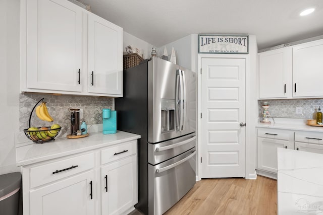 kitchen featuring light wood-type flooring, light stone counters, stainless steel refrigerator with ice dispenser, and white cabinetry