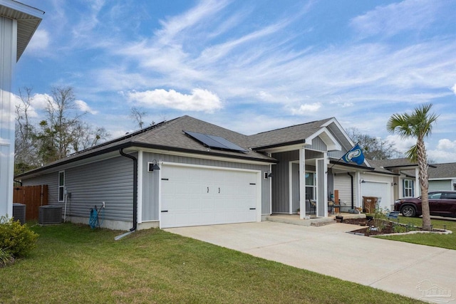 ranch-style house featuring an attached garage, roof mounted solar panels, cooling unit, driveway, and a front lawn