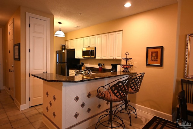 kitchen featuring pendant lighting, white cabinets, light tile patterned floors, kitchen peninsula, and stainless steel appliances