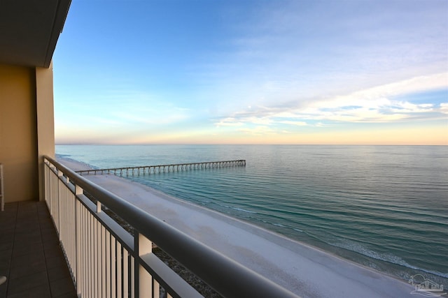 balcony at dusk featuring a beach view and a water view