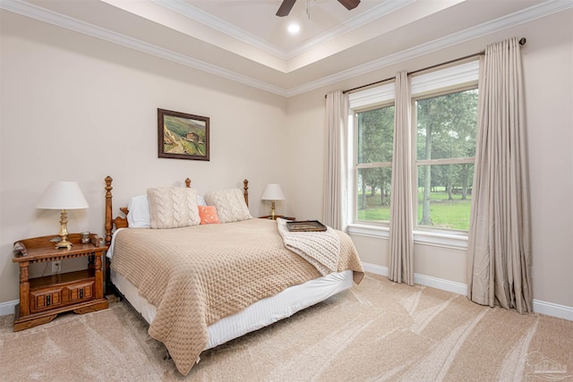 carpeted bedroom with a tray ceiling, multiple windows, ceiling fan, and ornamental molding