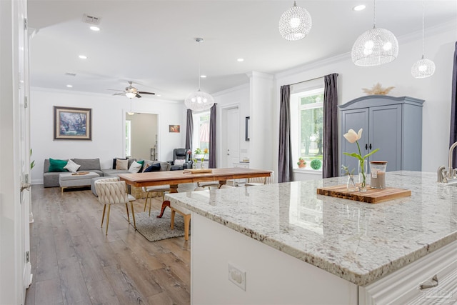 kitchen featuring decorative light fixtures, ceiling fan, crown molding, light stone counters, and light hardwood / wood-style flooring