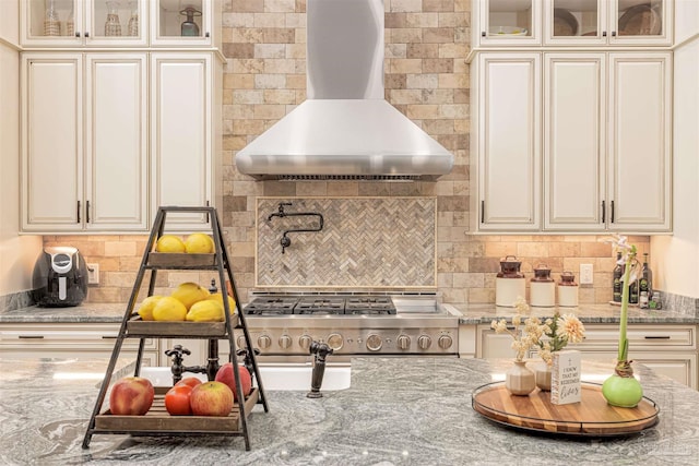 kitchen with range with gas stovetop, tasteful backsplash, cream cabinetry, wall chimney exhaust hood, and light stone countertops