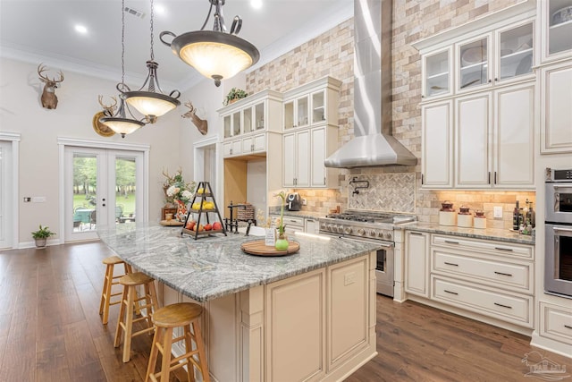 kitchen featuring wall chimney range hood, stainless steel appliances, crown molding, backsplash, and dark wood-type flooring