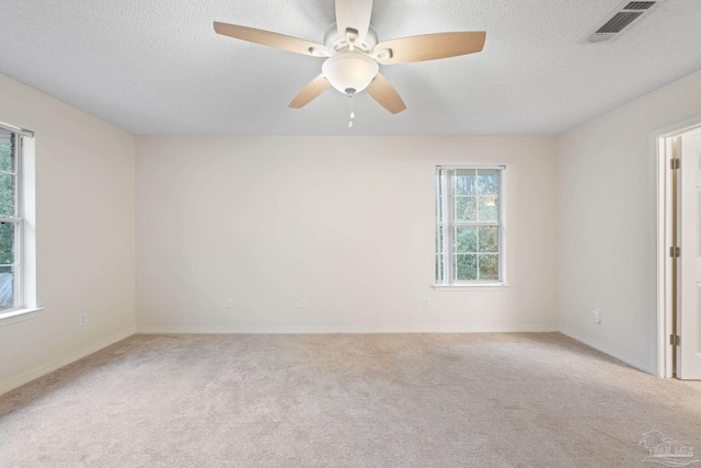 spare room with a textured ceiling, light colored carpet, and ceiling fan