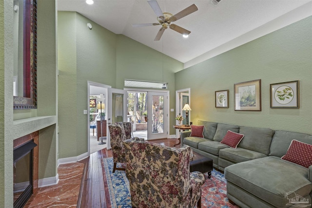 living room with dark wood-style floors, a ceiling fan, baseboards, high vaulted ceiling, and a brick fireplace