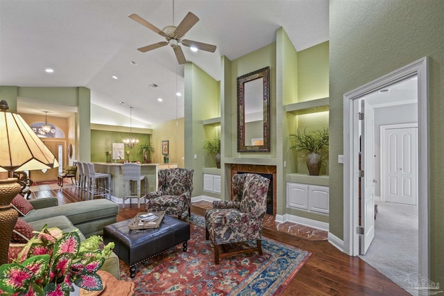 living area featuring built in shelves, baseboards, ceiling fan with notable chandelier, wood finished floors, and high vaulted ceiling