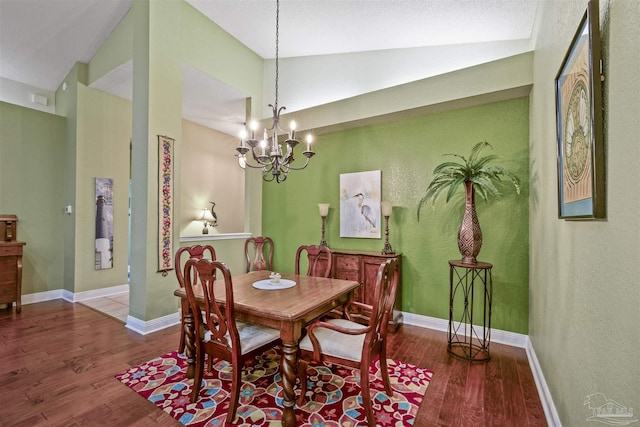 dining room featuring a notable chandelier, baseboards, lofted ceiling, and wood finished floors