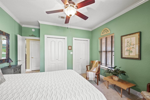 bedroom featuring visible vents, multiple closets, crown molding, carpet flooring, and baseboards