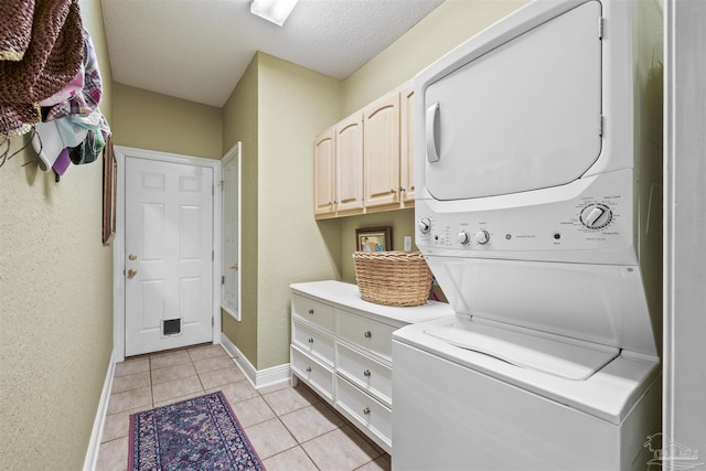 laundry room featuring baseboards, light tile patterned flooring, cabinet space, a textured ceiling, and stacked washer / drying machine