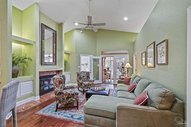 living room featuring built in features, high vaulted ceiling, a fireplace with flush hearth, ceiling fan, and hardwood / wood-style flooring