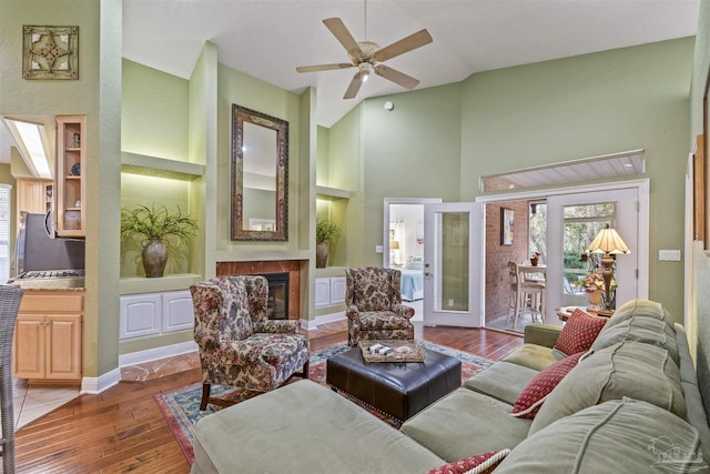 living area with built in features, wood finished floors, high vaulted ceiling, ceiling fan, and a glass covered fireplace