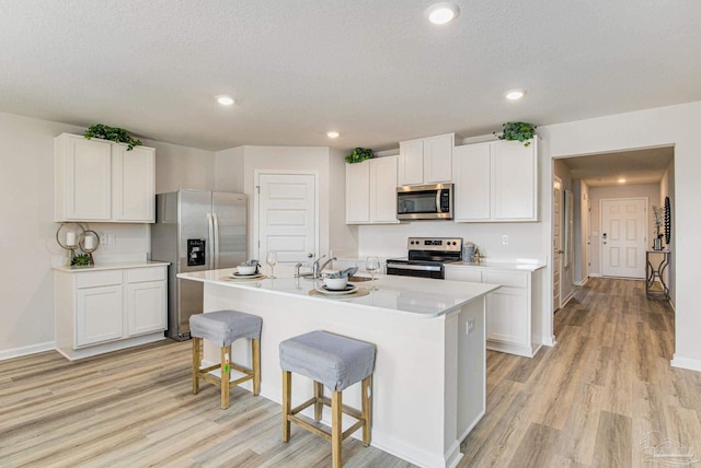 kitchen with a breakfast bar, stainless steel appliances, a center island with sink, light hardwood / wood-style flooring, and white cabinetry