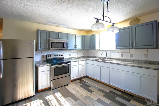 kitchen featuring backsplash, sink, hanging light fixtures, appliances with stainless steel finishes, and light hardwood / wood-style floors