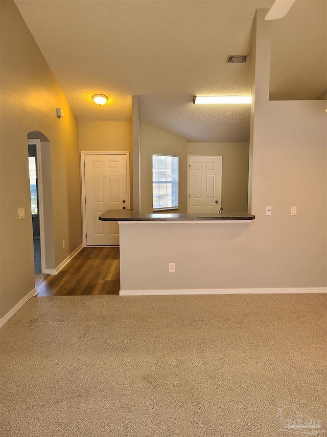 empty room with baseboards, visible vents, arched walkways, a textured ceiling, and dark colored carpet