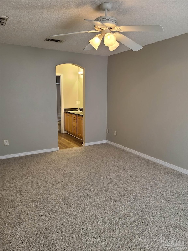 empty room featuring arched walkways, visible vents, light carpet, and baseboards