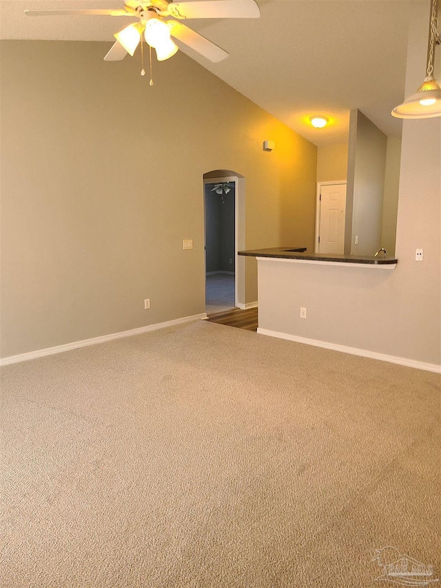 carpeted spare room featuring lofted ceiling, baseboards, arched walkways, and ceiling fan