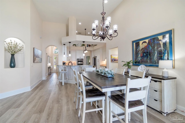 5136 Point Shores Ln, Gulf Breeze, FL 32563 - dining area with an inviting chandelier, a towering ceiling, baseboards, light wood-type flooring, and arched walkways