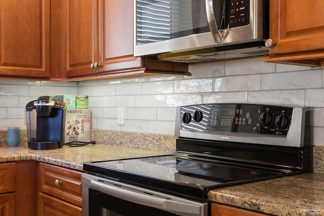 kitchen featuring tasteful backsplash, appliances with stainless steel finishes, brown cabinetry, and light stone counters