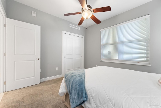 bedroom featuring a closet, light colored carpet, visible vents, a ceiling fan, and baseboards