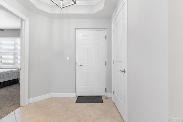 foyer entrance featuring light tile patterned floors, baseboards, light colored carpet, ornamental molding, and a tray ceiling