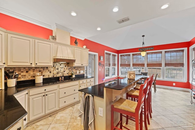 kitchen with lofted ceiling, a breakfast bar, hanging light fixtures, a kitchen island, and cream cabinetry