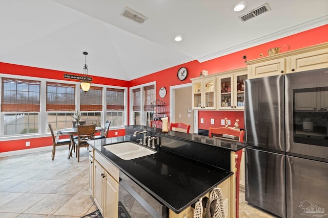 kitchen with sink, stainless steel fridge, cream cabinets, an island with sink, and vaulted ceiling