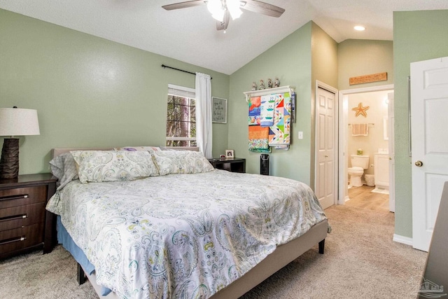 bedroom featuring ceiling fan, vaulted ceiling, ensuite bath, light carpet, and a closet