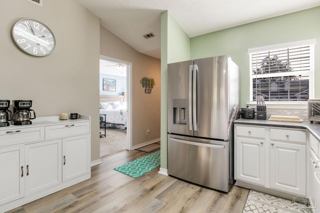 kitchen with vaulted ceiling, light wood-type flooring, stainless steel fridge with ice dispenser, a textured ceiling, and white cabinets